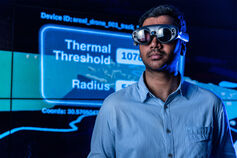 A student wearing virtual reality glasses stands in front of a digital display.